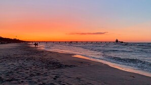 Uma praia com um píer que se estende para o oceano ao pôr do sol.