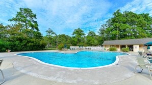 Una piscina de borde curvo, rodeada por una terraza de concreto y sillas de descanso.