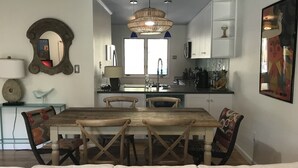 Una cocina moderna con una isla central, armarios blancos y una zona de comedor con mesa y sillas de madera.