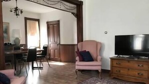 A living room with a pink armchair, a television on a wooden stand, a dining area with a table and chairs, and a patterned rug. - Charming home in the heart of Rockland, Charming home in the heart of Rockland (Rockland)