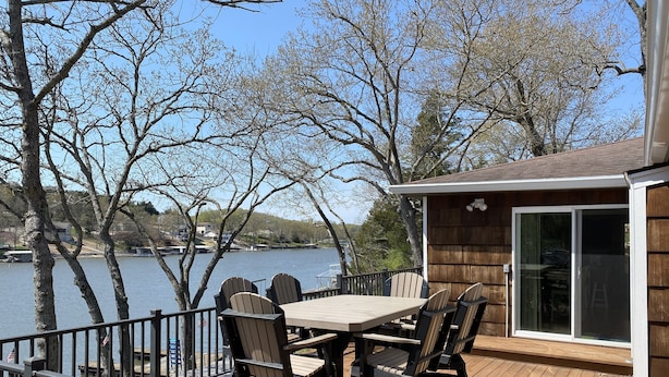 A deck with a table and chairs overlooking a lake, surrounded by trees. - Single level home in a gentle, quiet , deep water cove  at Lake of the Ozarks . (Roach)