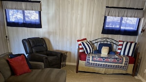 A living room with a brown sofa, a black armchair, and a bed with a striped pillow. - Single level home in a gentle, quiet , deep water cove  at Lake of the Ozarks . (Roach)