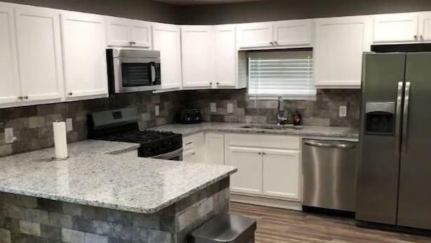 Una cocina moderna con armarios blancos, encimera de granito, refrigerador de acero inoxidable y salpicadero de piedra.