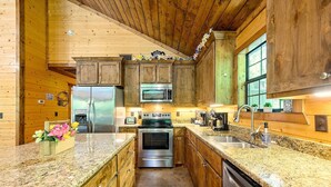 A kitchen with wooden cabinets, granite countertops, stainless steel appliances, and a window. - The Blue Heron, HIDDEN IN THE WOODS YET CLOSE TO TOWN (Broken Bow)