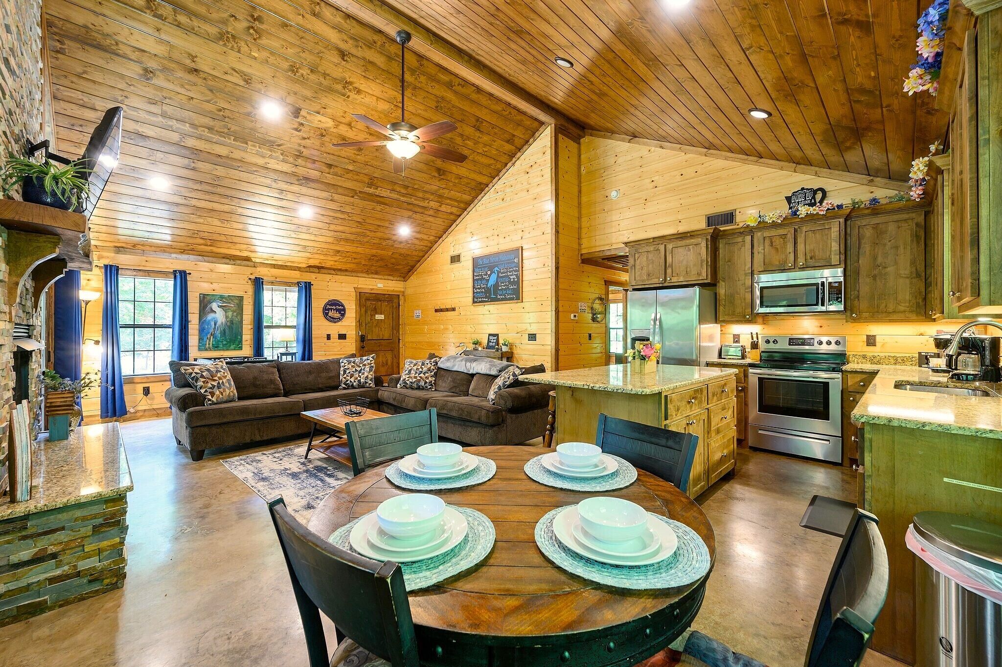 A spacious living area with a wooden ceiling, a dining table set with plates, a sofa, and a kitchen with modern appliances.