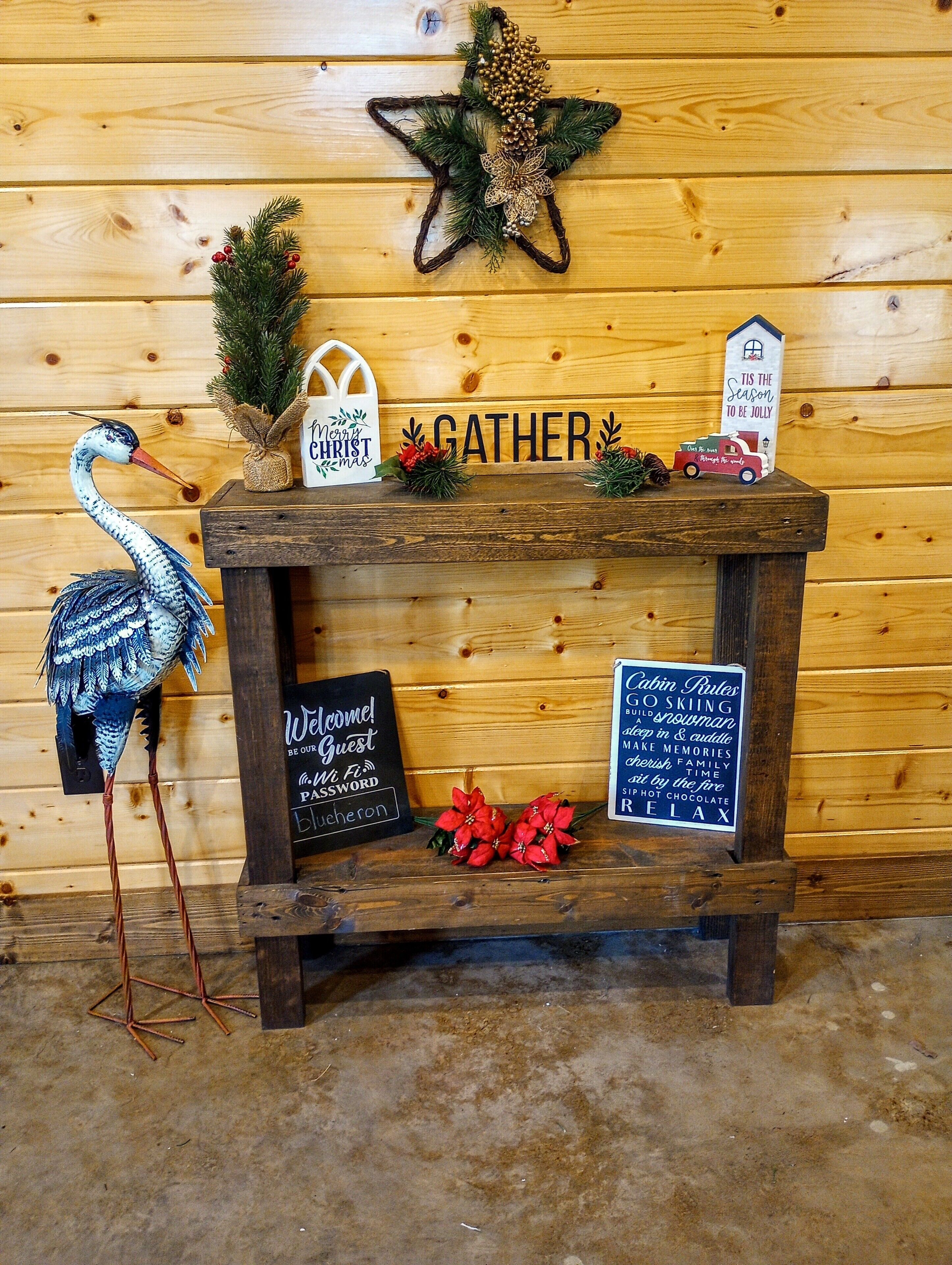 Un banc en bois orné d’une étoile, une pancarte en bois avec le mot « GATHER » (rassemblement), une pancarte en bois avec la phrase « Tis the Season to be Jolly » (c’est le moment de faire la fête), une pancarte en bois avec la phrase « Cabin Rules » (règles de la cabane), une pancarte en bois avec la phrase « Welcome! Be our Guest » (bienvenue, soyez nos invités) et une pancarte en bois avec le mot « Password » (mot de passe).