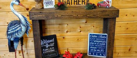 Un banc en bois orné d’une étoile, une pancarte en bois avec le mot « GATHER » (rassemblement), une pancarte en bois avec la phrase « Tis the Season to be Jolly » (c’est le moment de faire la fête), une pancarte en bois avec la phrase « Cabin Rules » (règles de la cabane), une pancarte en bois avec la phrase « Welcome! Be our Guest » (bienvenue, soyez nos invités) et une pancarte en bois avec le mot « Password » (mot de passe).