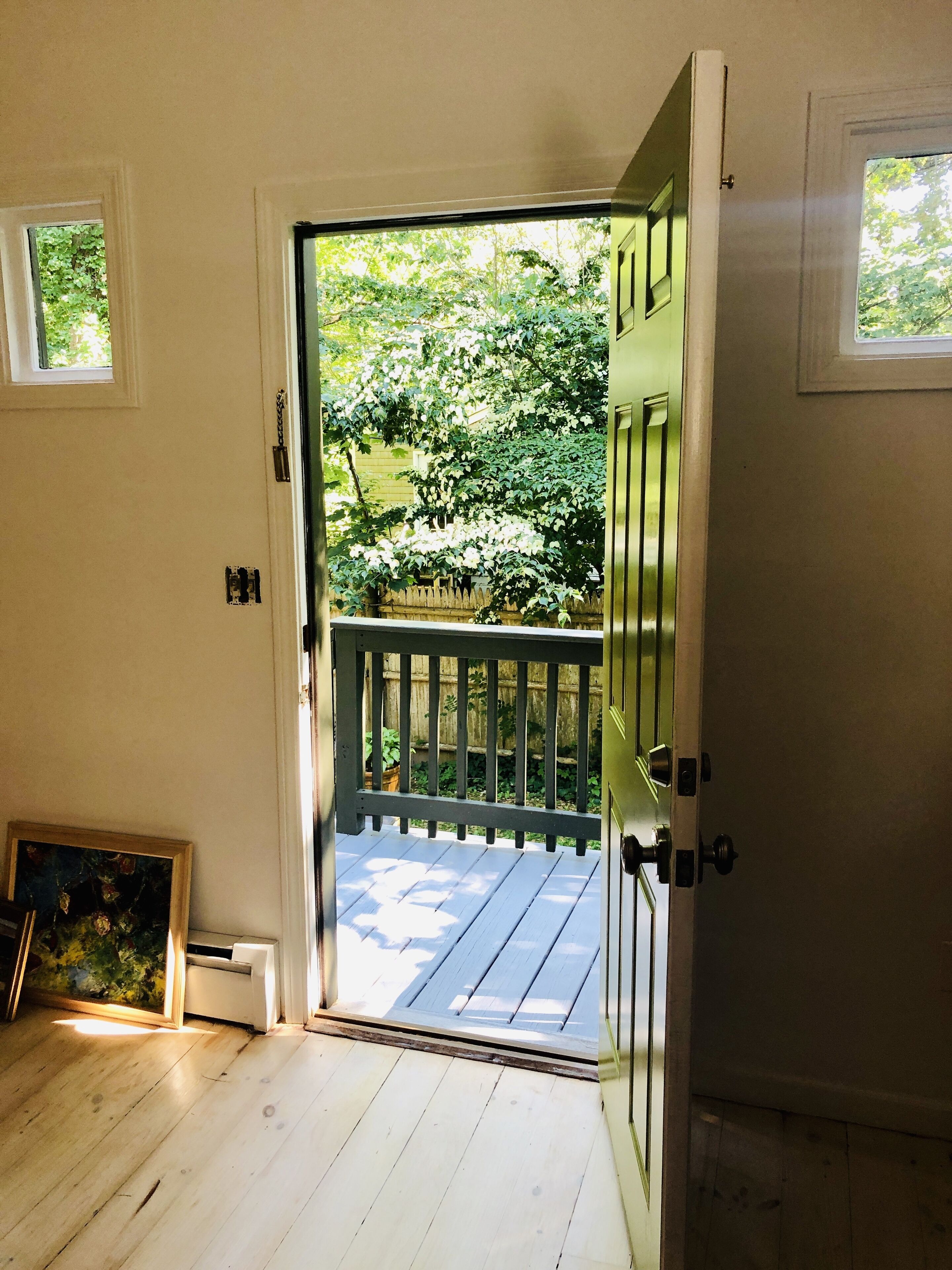Una habitación con piso de madera, una puerta que da a una terraza exterior con barandilla y una ventana pequeña en la pared.