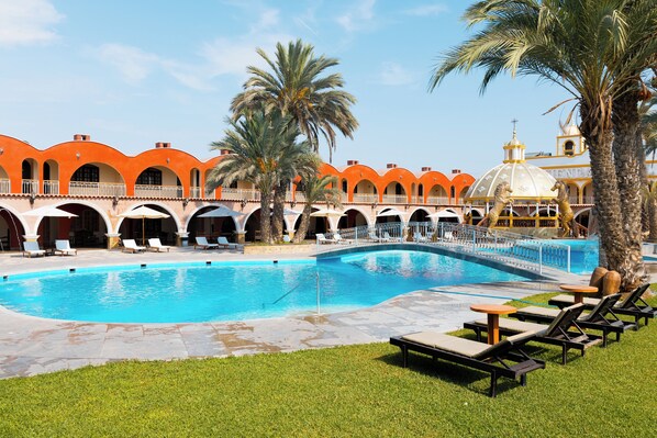 Une piscine avec des chaises longues et des palmiers.
