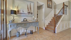 Een trap met een houten leuning en zwarte spijbels, een witte deur, en een schilderij van zeilboten aan de muur.