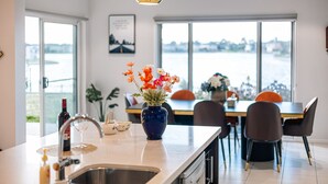 A modern kitchen with a large window, a vase of flowers, and a dining area with chairs and a table. - Lakefront villa with a spacious panoramic balcony in Sanctuary Lakes (Point Cook)