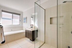 A modern bathroom with a glass shower enclosure, a bathtub, and a vanity with a mirror.