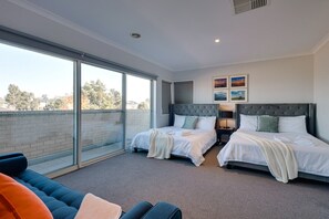A modern bedroom with two beds, large windows, and a balcony.
