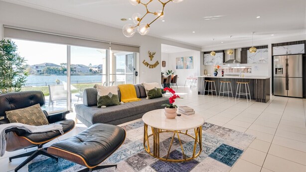 A modern living room with a sofa, a coffee table, and a view of a body of water. - Lakefront villa with a spacious panoramic balcony in Sanctuary Lakes (Point Cook)