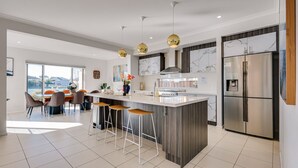 A modern kitchen with a central island, bar stools, stainless steel appliances, and pendant lighting. - Lakefront villa with a spacious panoramic balcony in Sanctuary Lakes (Point Cook)