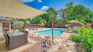 Un jardin avec une piscine, une terrasse en bois, du mobilier d’extérieur et un espace ombragé.