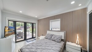 Une chambre moderne équipée d’un lit, d’une télévision, d’un bureau et d’une porte-fenêtre coulissante donnant sur une terrasse.