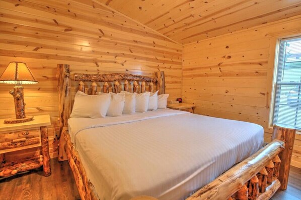 A wooden cabin bedroom with a bed, a nightstand, a lamp, and a window.