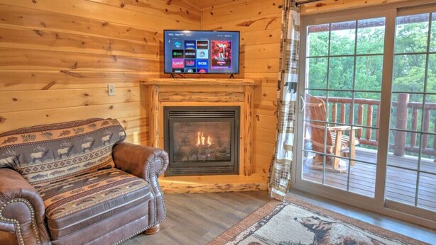 A cozy cabin interior with a fireplace, a leather sofa, and a TV mounted above it. - Cozy Lodge Suite with Kitchen in Amish Country (Millersburg)