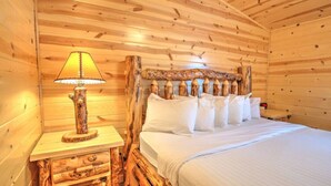 A wooden cabin room with a bed, a nightstand, and a lamp. - Cozy Lodge Suite with Kitchen in Amish Country (Millersburg)