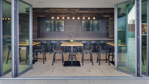 A modern dining area with a wooden table and chairs, a central sink, and large windows.