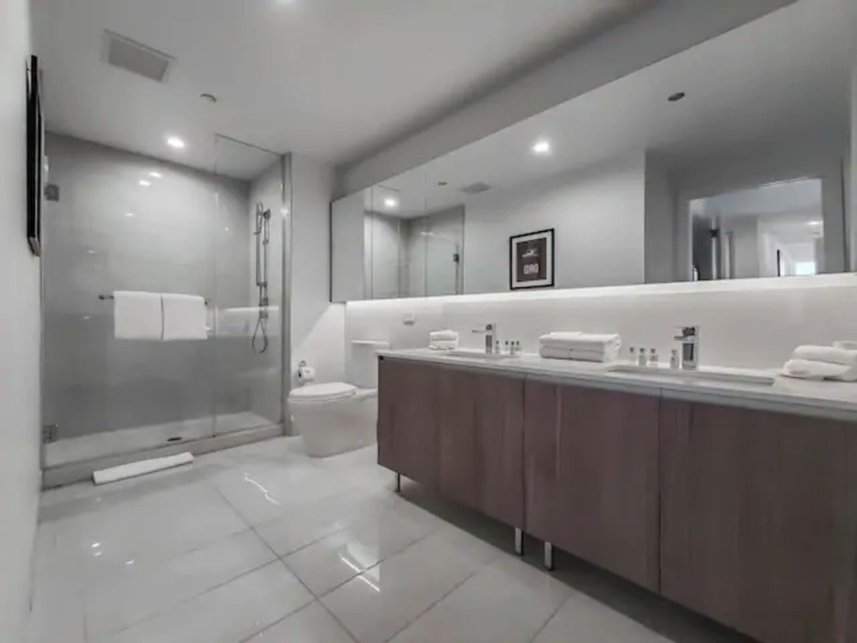 A modern bathroom with a glass-enclosed shower, a large mirror, and a vanity with toiletries.