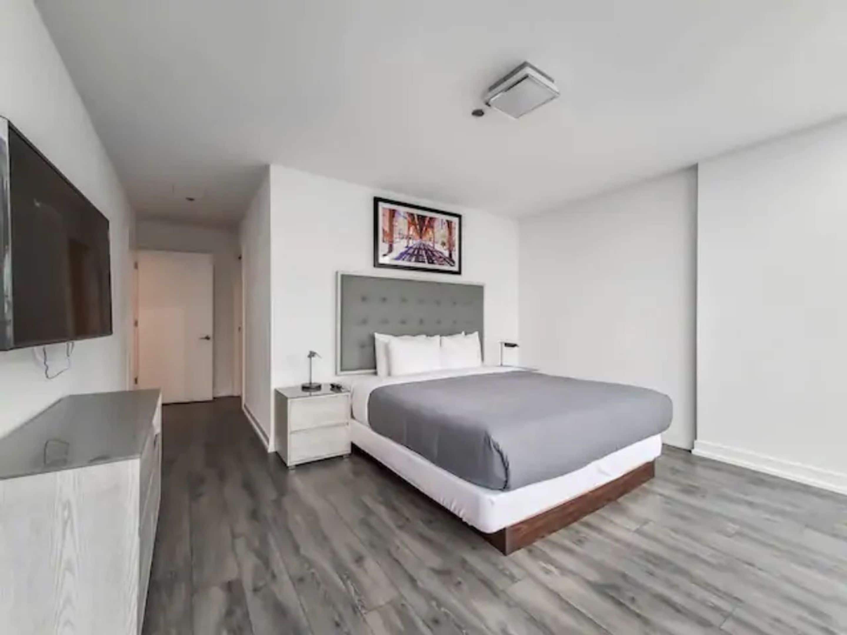 Et moderne hotelværelse med en stor seng, et fladskærms-tv, et natbord og et billede på væggen.