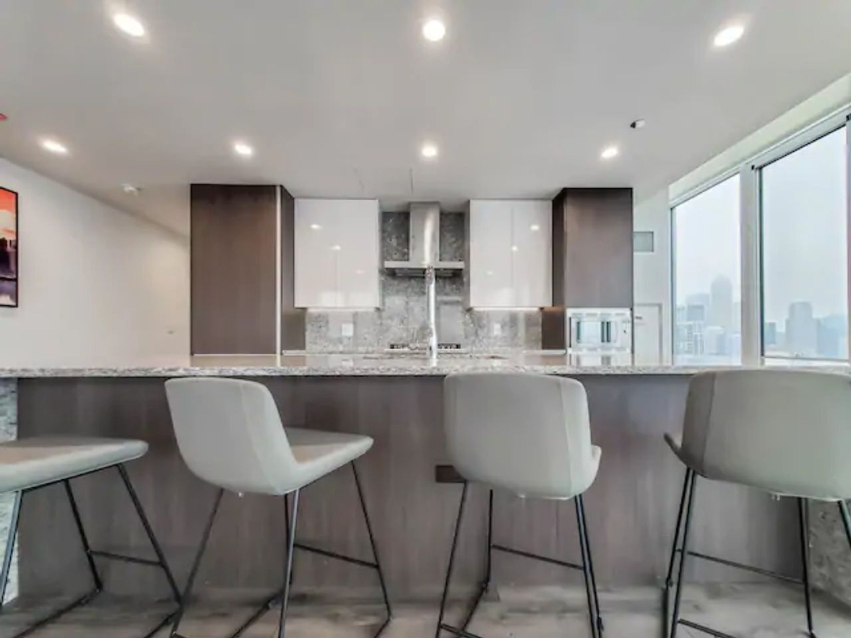 Cozinha moderna com ilha central, banquetas e vista para a cidade através de grandes janelas.