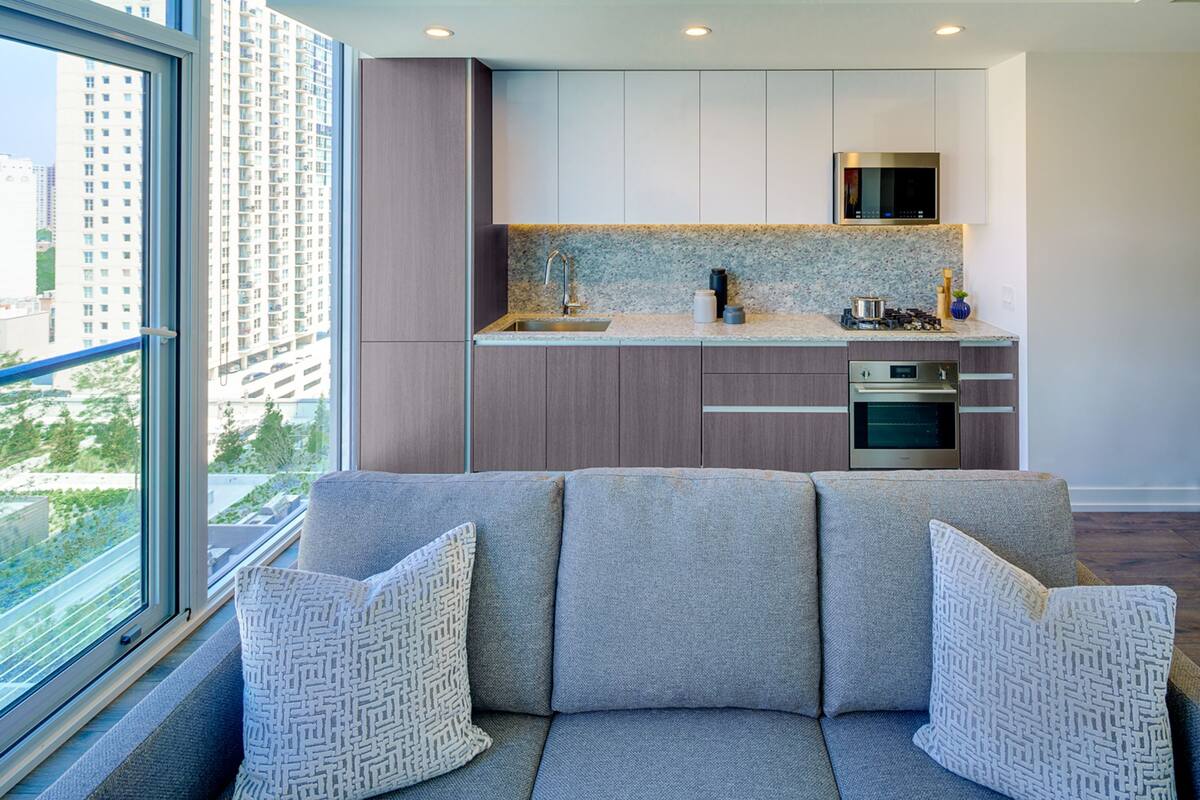 A modern kitchen with a built-in oven, a microwave, and a sink. There is a window with a view of a cityscape.