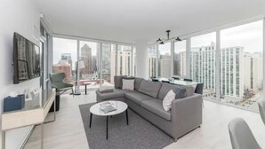A modern living room with a grey sectional sofa, a round coffee table, and a glass desk with a chair. Large windows offer a city view. - Level Chicago – Old Town (Chicago)