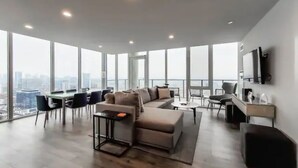 A spacious living area with a large sofa, a dining table, and a TV mounted on the wall.
