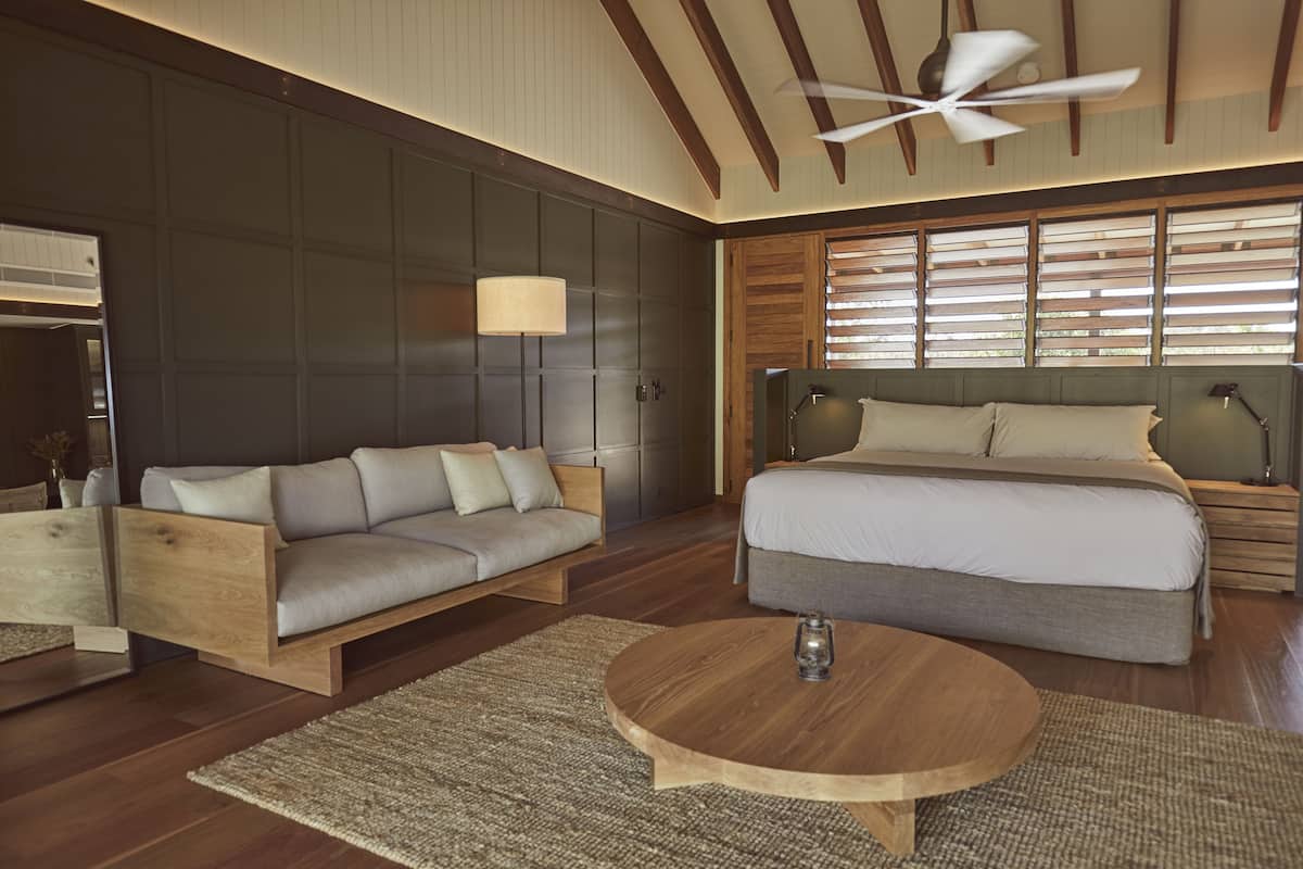 A modern bedroom with a large bed, a sofa, a wooden coffee table, and a ceiling fan.