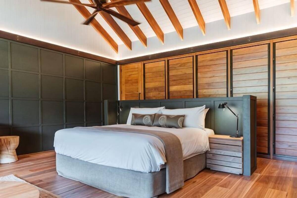 A modern bedroom with a large bed, built-in headboard, and a wooden ceiling.