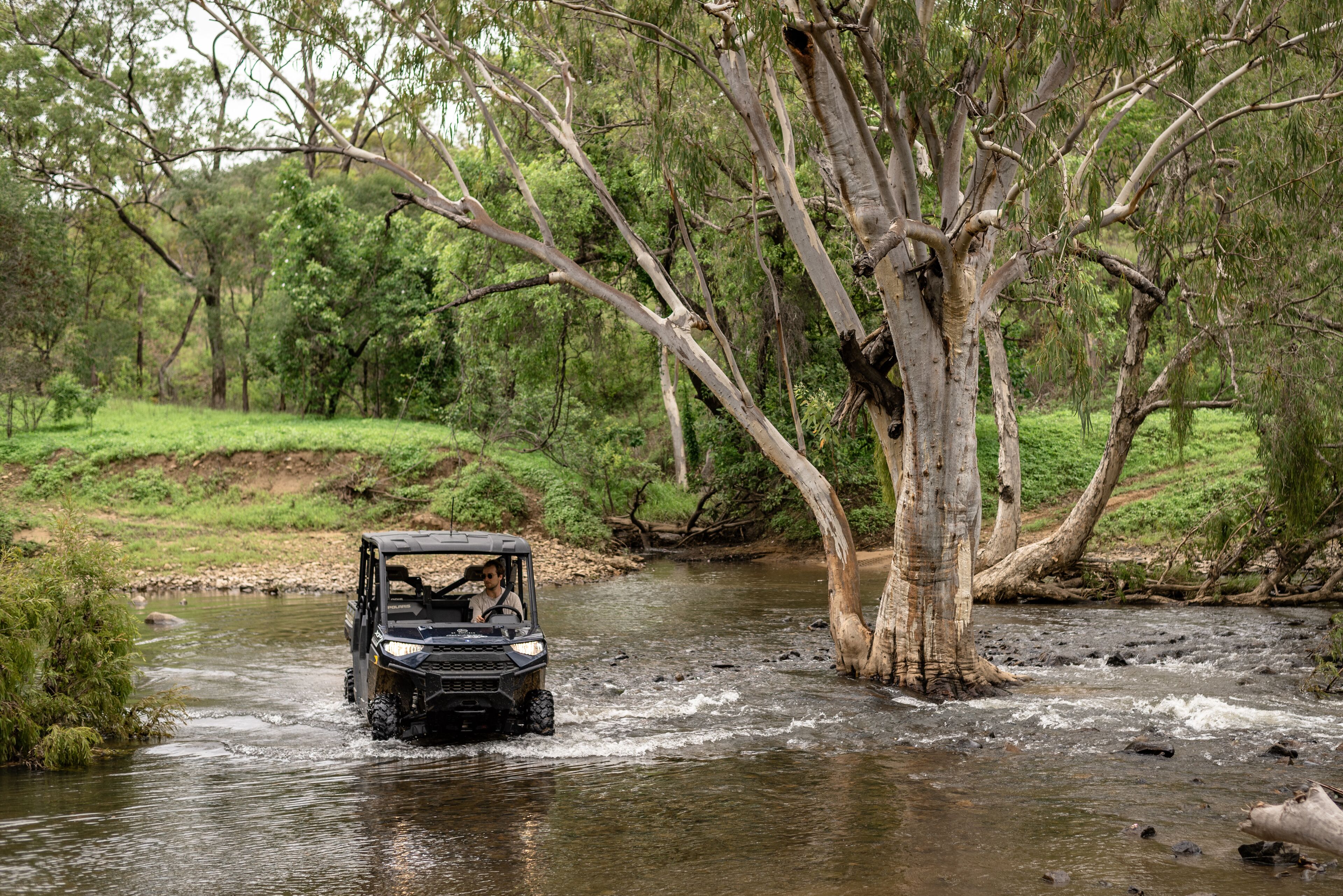 A vehicle navigating a river surrounded by trees.