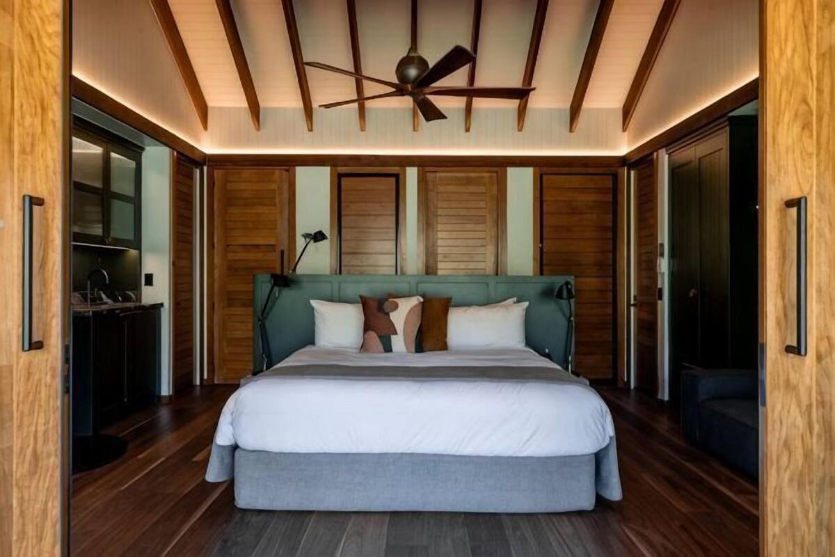 A bedroom with a large bed, wooden ceiling beams, and a ceiling fan.