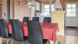 Un comedor con una mesa roja y sillas negras, una cocina con armarios blancos y un techo de madera.