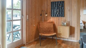 Una habitación con paredes de madera, una silla de mimbre, un mueble pequeño y una exposición de conchas marinas en la pared.