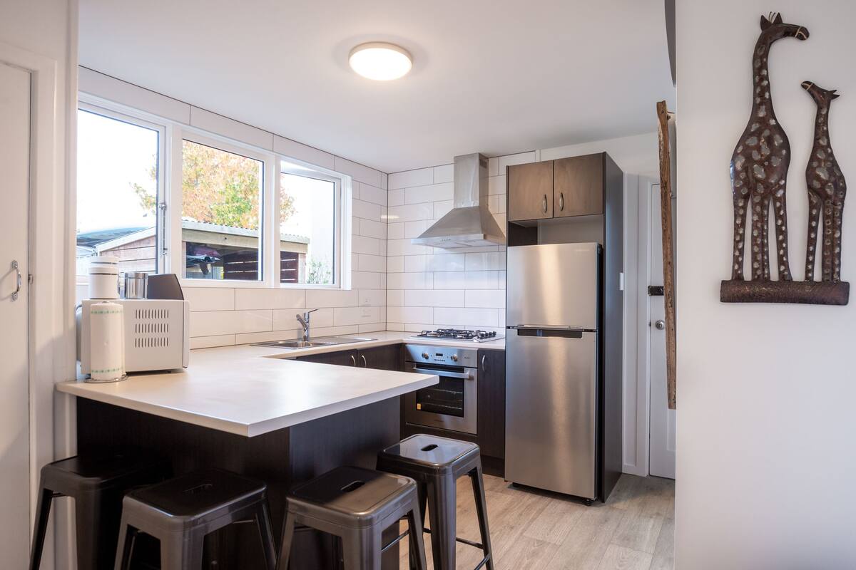 A modern kitchen with white tiles, stainless steel appliances, and a large window.