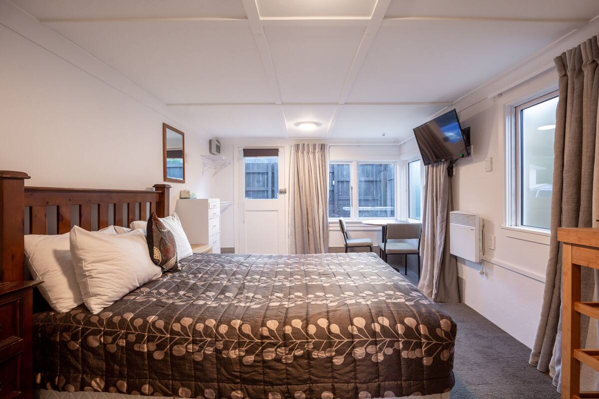 A hotel room with a large bed, a desk, a television, and a window with curtains.
