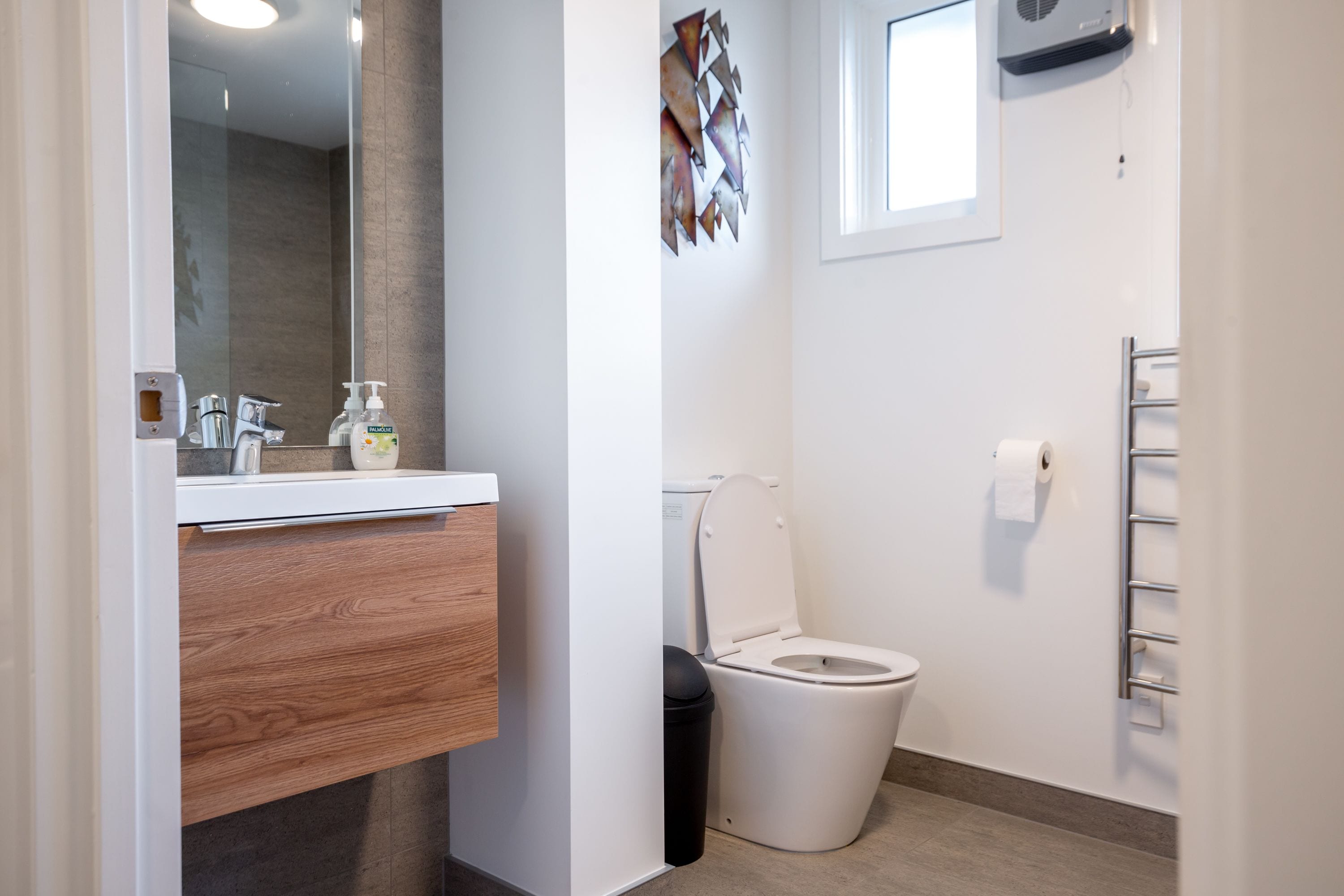 Une salle de bain moderne avec un meuble-lavabo en bois, des toilettes blanches et un porte-serviettes.