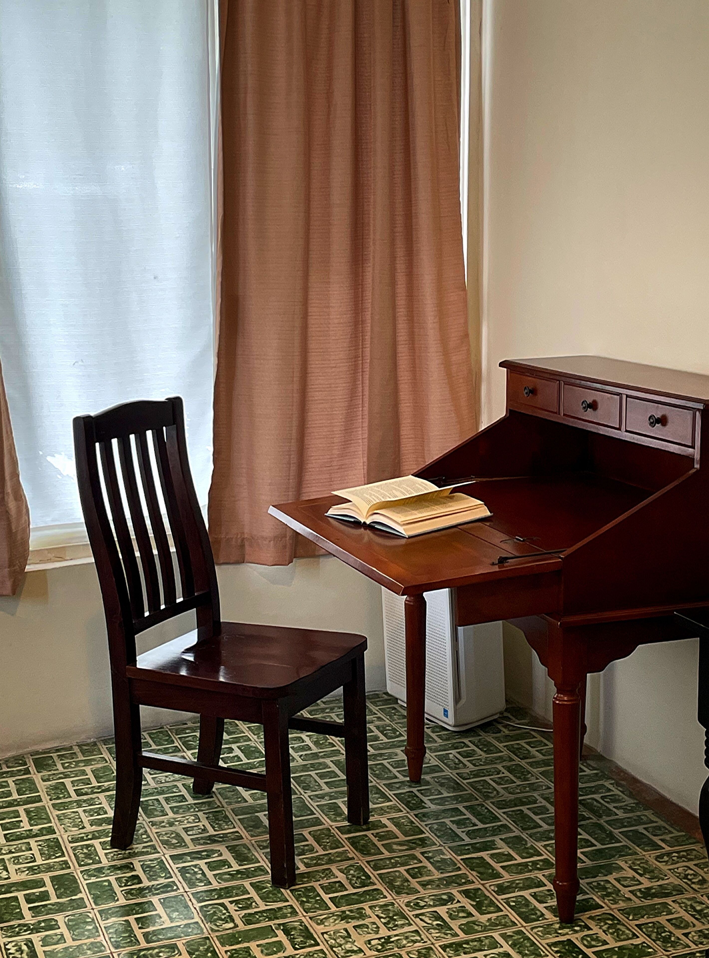 A room with a wooden desk, a chair, and a window with curtains.