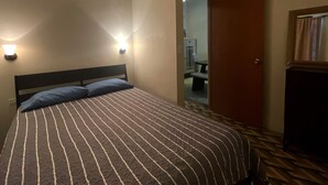 Habitación de hotel con cama, dos lámparas adosadas a la pared, una puerta y una pequeña mesa con sillas al fondo.