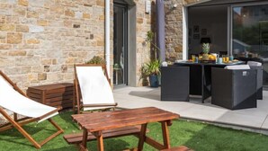 Un patio con mesa y sillas de madera, una silla de lona blanca y un muro de piedra.