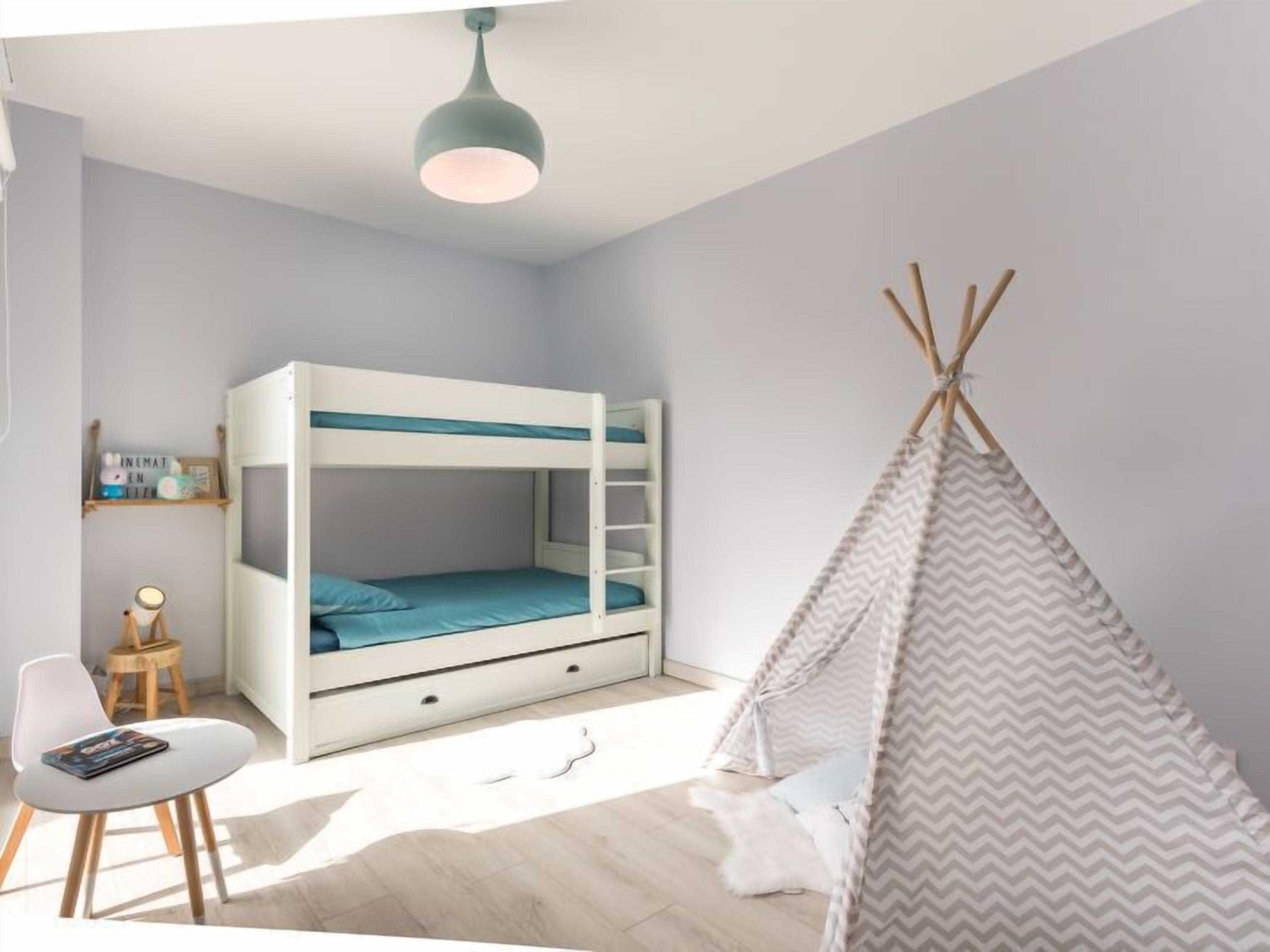 A child's bedroom with a bunk bed, a small table, a chair, a hanging light fixture, and a teepee tent.