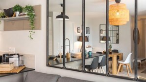 Una sala de estar moderna con un espejo grande, un comedor con mesa y sillas de madera, y una lámpara colgante.