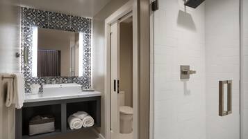 Un baño moderno con un lavamanos blanco, un espejo con diseño, una ducha con cabezal de ducha de mano y un inodoro.