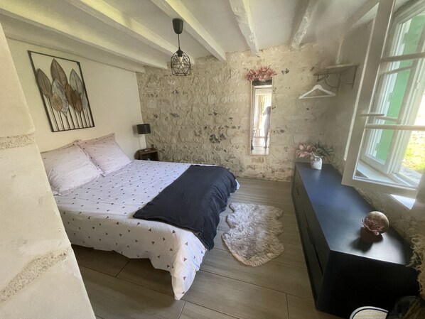 Un dormitorio con cama, mesita de noche, cómoda, ventana y pared de piedra.