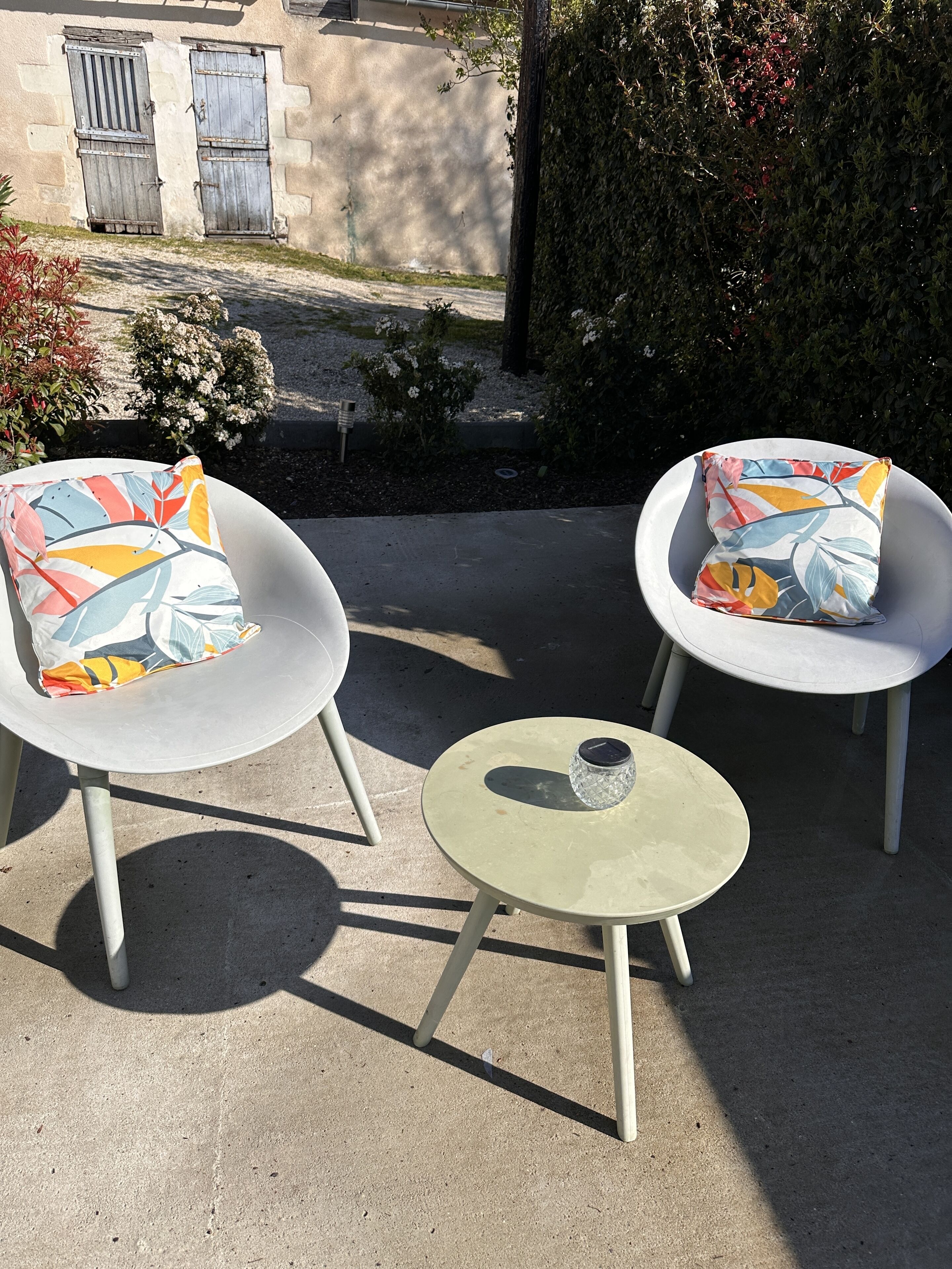 Two white armchairs with colorful cushions and a small round table with a glass container.