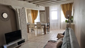 Ett vardagsrum med en TV, en soffa, en matplats med stolar och ett bord.