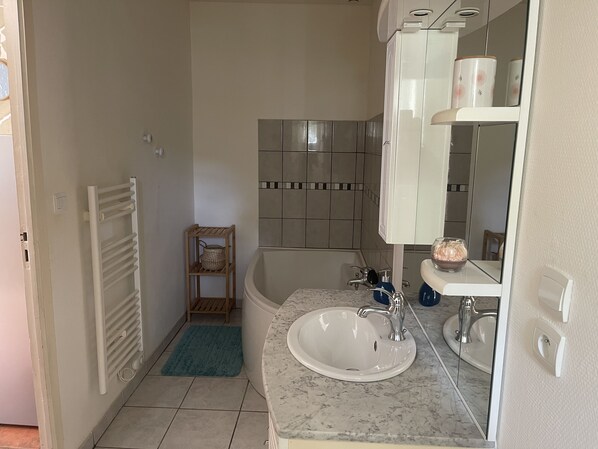 Un baño con bañera, lavamanos, espejo y toallero.